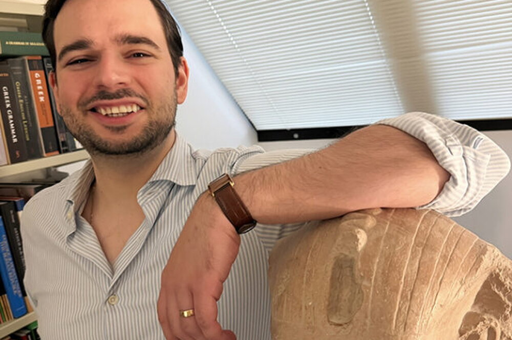 Eduardo stands in his office with his arm resting on a replica of an ancient portrait bust,