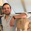 Eduardo stands in his office with his arm resting on a replica of an ancient portrait bust,