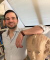 Eduardo stands in his office with his arm resting on a replica of an ancient portrait bust,